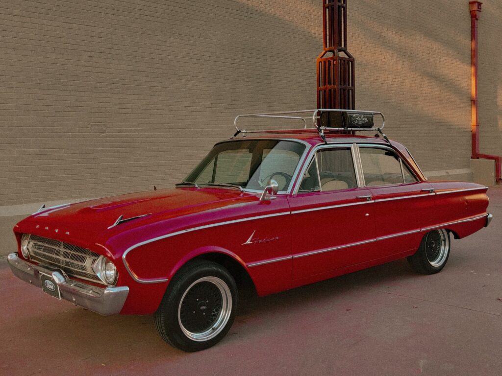 Classic red Ford sedan with roof rack against brick wall backdrop.